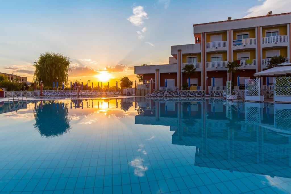 uma piscina em frente a um hotel com o pôr do sol em Hotel Olympus em Caorle