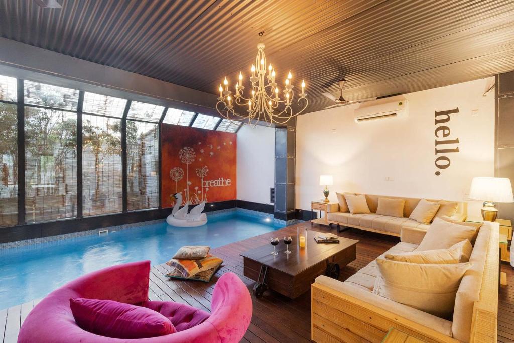 een woonkamer met een zwembad in het midden bij StayVista's The Barn House - Farm-View Villa with Modern Rustic Interiors, Indoor Pool & Bar in Chandīgarh