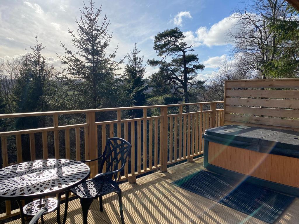 eine Holzterrasse mit einem Tisch und Stühlen sowie einem Tisch und einem Tisch in der Unterkunft Beechnut Lodge with Hot Tub in Cupar