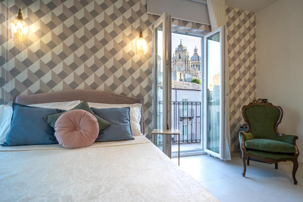 a bedroom with a bed and a chair and a window at Maiolica Rooms in Ragusa