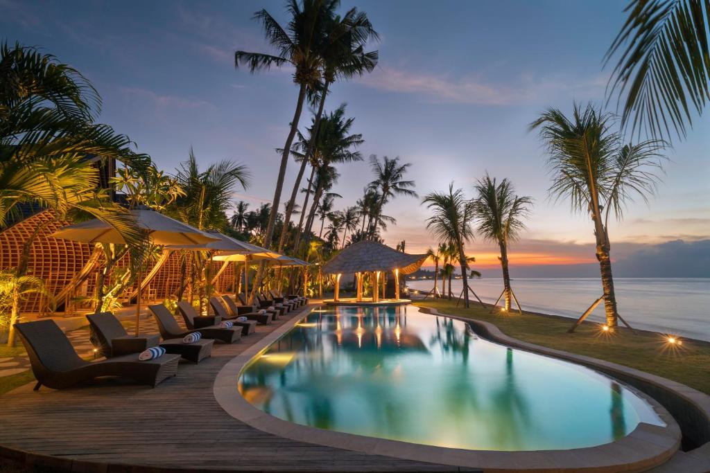 een zwembad met ligstoelen en de oceaan bij zonsondergang bij The Sankara Beach Resort - Nusa Penida in Nusa Penida