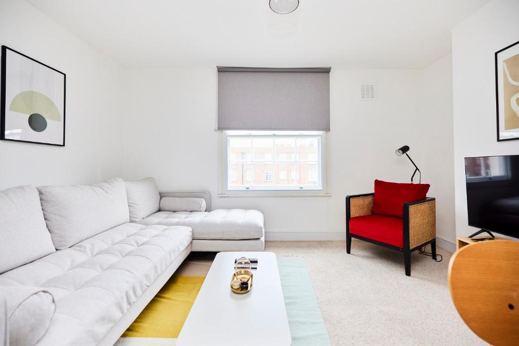 uma sala de estar com um sofá branco e uma cadeira vermelha em The Clapham Getaway - Charming 1BDR Flat em Londres