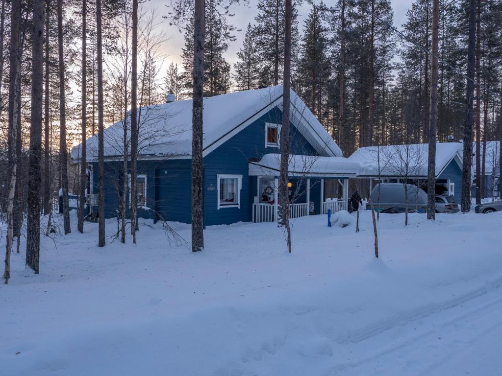 a blue house with a snow covered roof in the woods at Villa Vilttitossu in Äkäslompolo