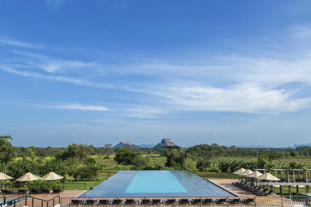 a large swimming pool with chairs and umbrellas at Aliya Resort and Spa - Thema Collection in Sigiriya