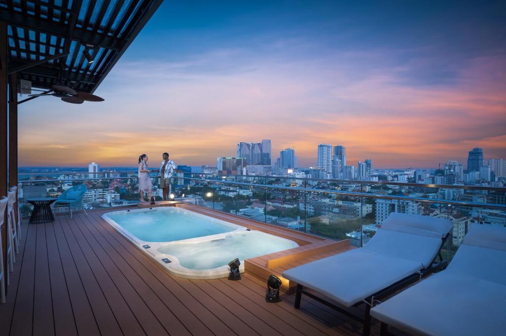 two people standing on the deck of a building with a swimming pool at Capri by Fraser, Phnom Penh in Phnom Penh