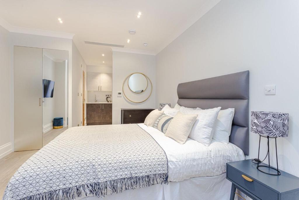 una camera bianca con un grande letto e uno specchio di Cleveland Residences Kensington a Londra