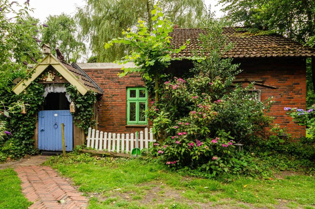een klein bakstenen huis met een blauwe deur en een hek bij Fairy Cottage in Rhauderfehn