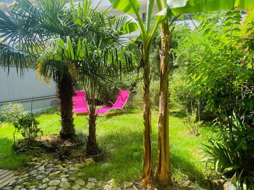 une chaise rose dans un jardin avec des palmiers dans l'établissement Le Galilée - Jardin privatif, à La Rochelle