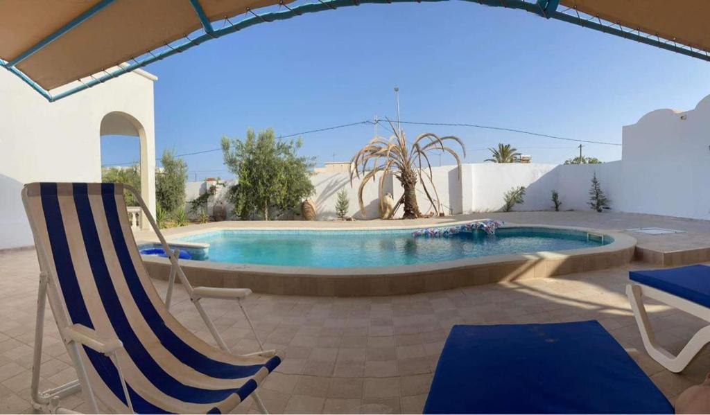 una piscina con una silla, una mesa y una silla en Waneshouse دار الونس (Djerba), 