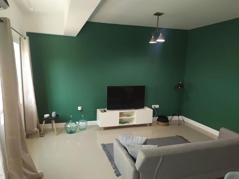 uma sala de estar com uma parede verde e uma televisão de ecrã plano em Homing Plateau - Apartment in the city of Praia em Praia