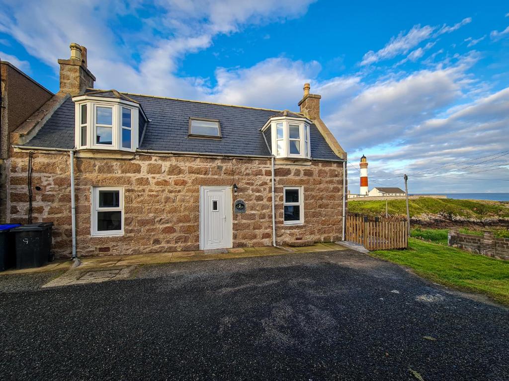 a stone house with a lighthouse in the background at Puffin Cottage in Boddam