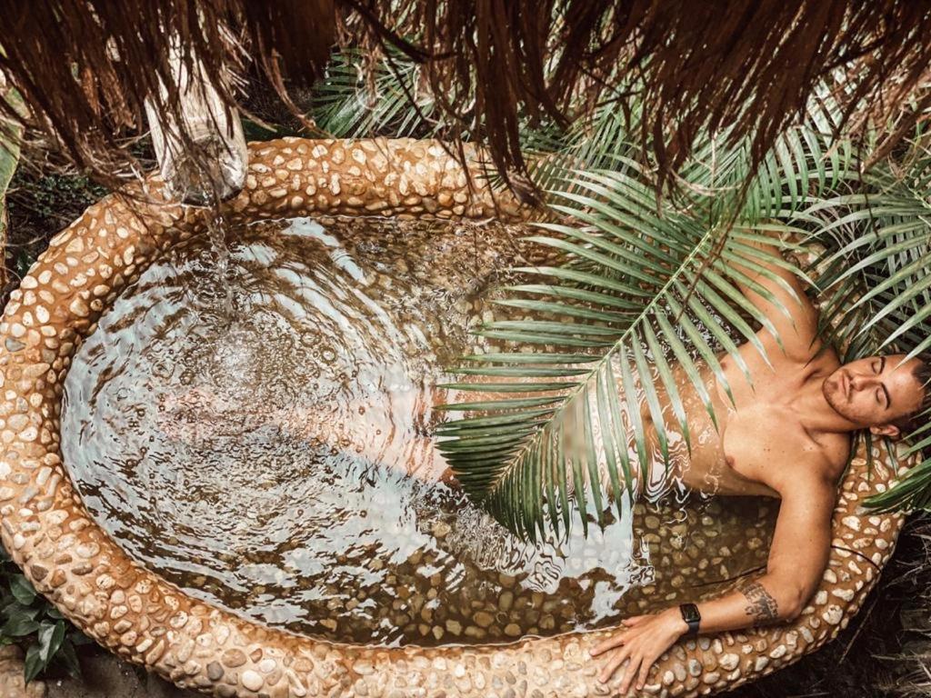 un homme se posant dans un bassin d'eau avec un palmier dans l'établissement Villa Fulô, à Caraíva