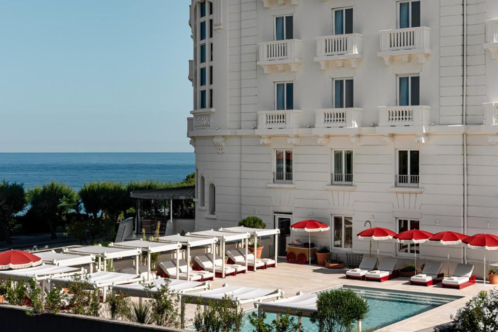 um hotel com piscina, cadeiras e guarda-sóis em Regina Experimental Biarritz em Biarritz