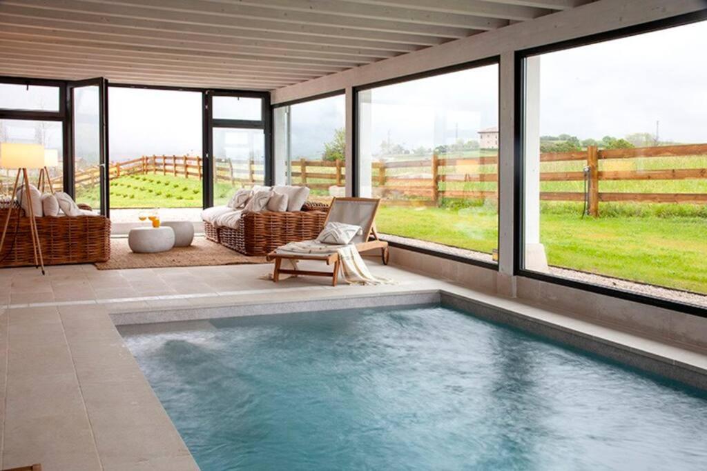 uma piscina numa sala de estar com janelas em Villa sublime con piscina climatizada y vistas em Prellezo