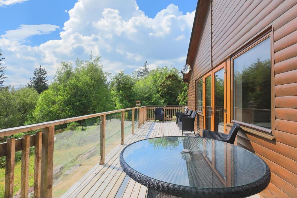 a wooden deck with a glass table and chairs on it at Honeysuckle, Colvend in Rockcliffe