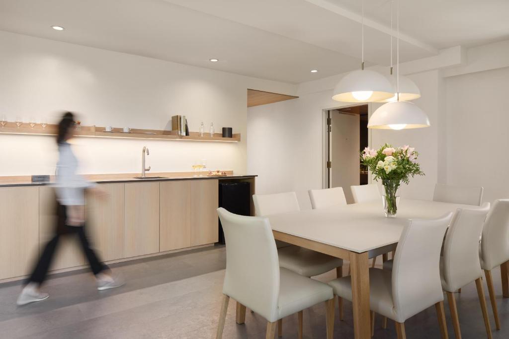 a woman walking past a dining room and kitchen with a table and chairs at Hôtel de l'ITHQ in Montréal