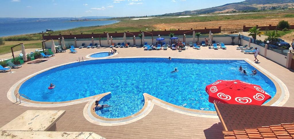 a large swimming pool with a red umbrella and people in it at Flora Hotel in Gelibolu