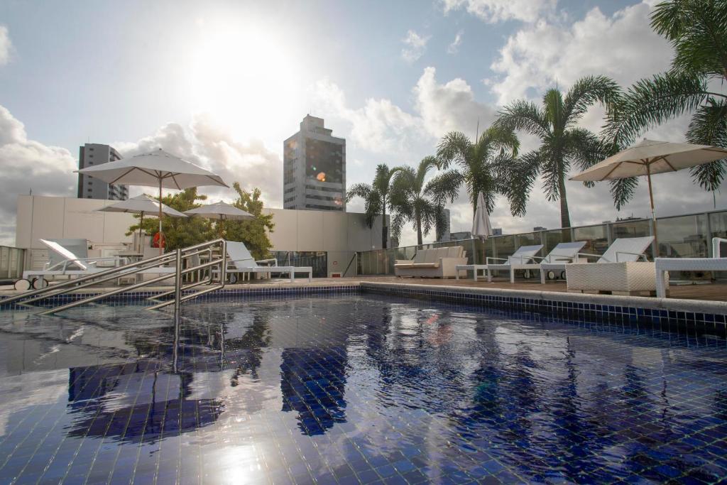 uma piscina com cadeiras e guarda-sóis num edifício em Bugan Recife Boa Viagem Hotel - by Atlantica no Recife