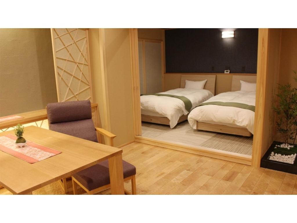 Zimmer mit 2 Betten, einem Tisch und einem Spiegel in der Unterkunft Unazuki Onsen Sanyanagitei - Vacation STAY 06522v in Kurobe