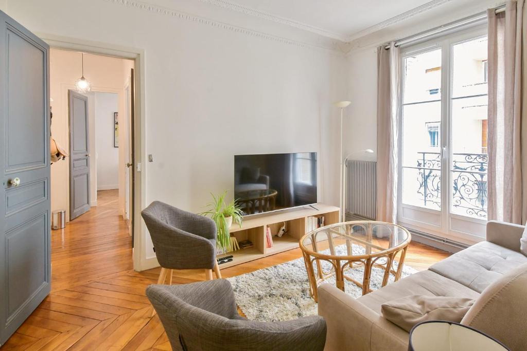 un salon avec un canapé, des chaises et une télévision dans l'établissement Appartement Haussman et son balcon - Welkeys, à Paris