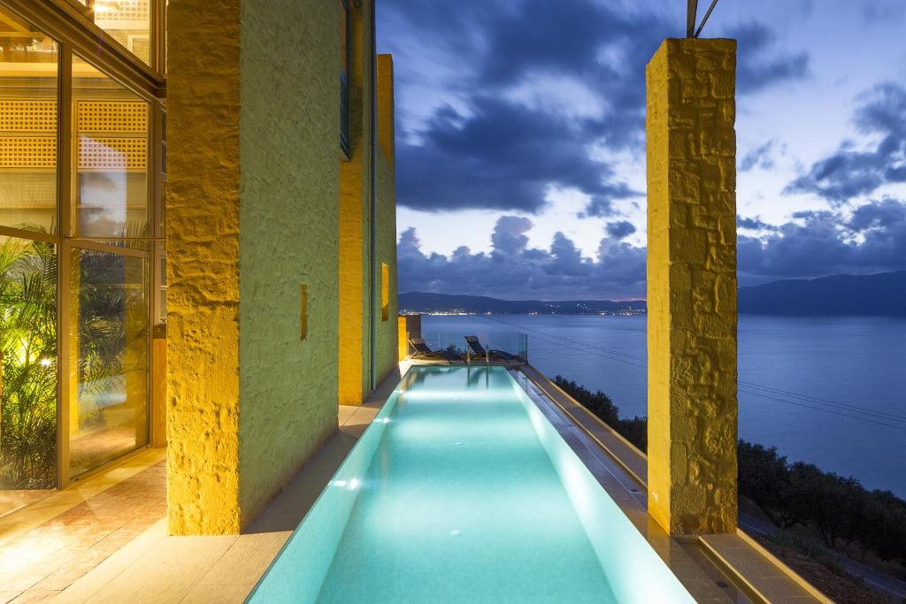 una piscina en un edificio con vistas al agua en Athina Epavlis - Ethereal Charm of Blue Horizons, en Ravdhoúkha