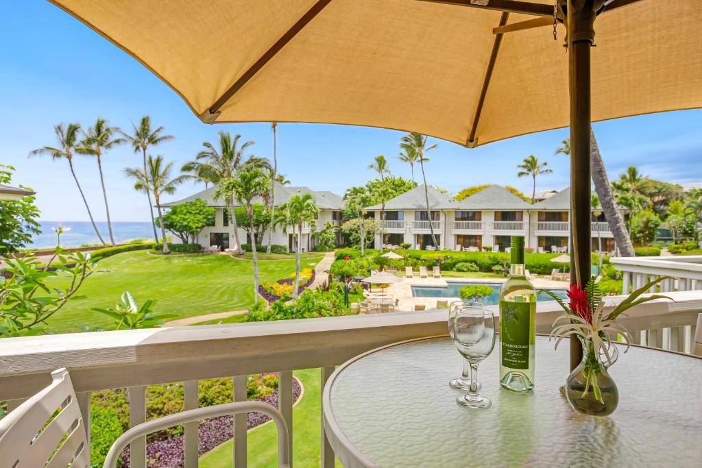 a table with wine glasses and an umbrella on a balcony at Top Floor Ocean View Condo at Poipu Kapili- Alekona Kauai in Koloa
