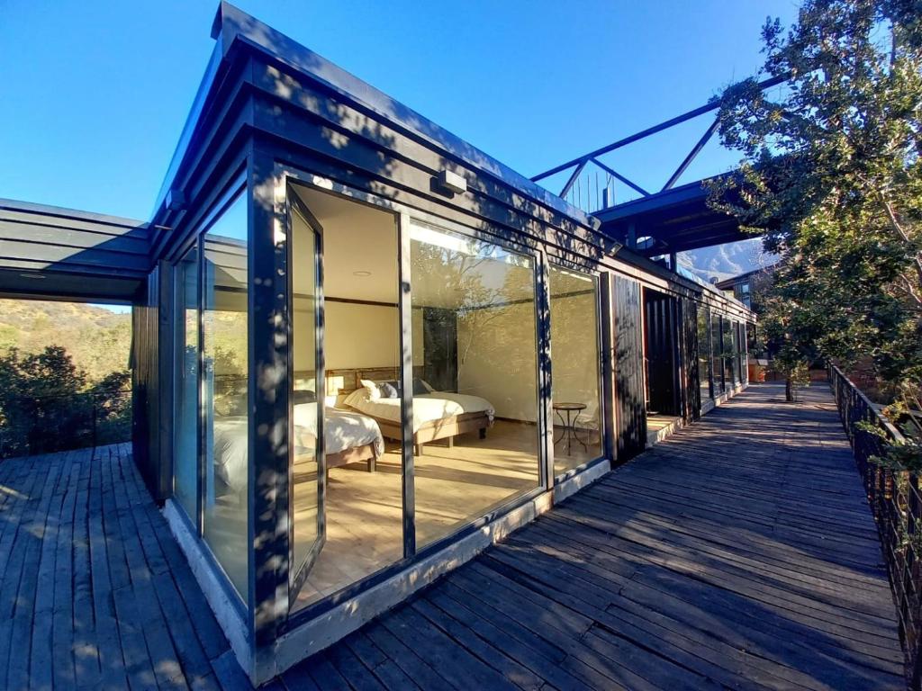 a glass house with a bedroom and a deck at Wine Lodge de Viña Vultur en bosque nativo con piscina in Doñihue