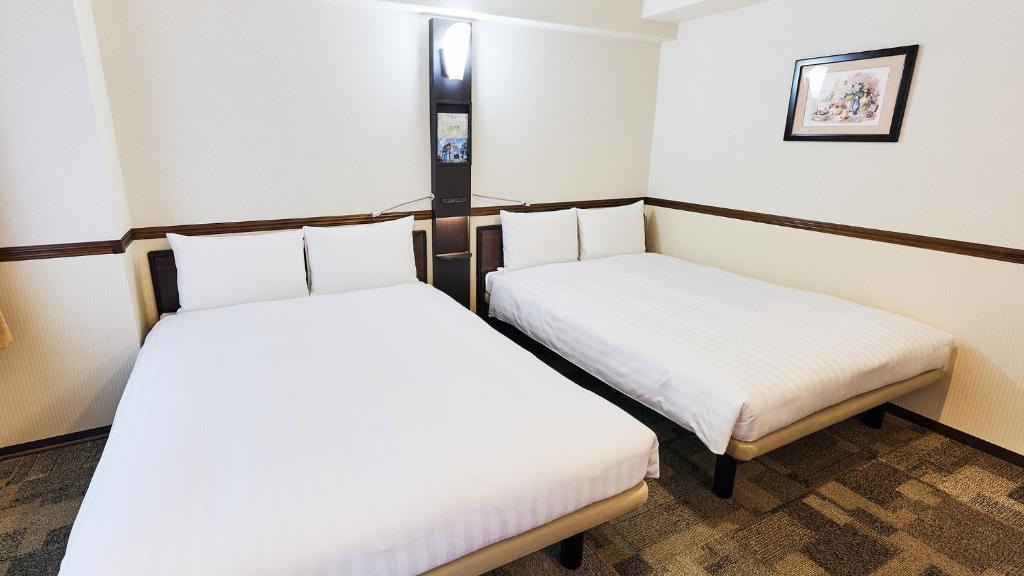 two beds in a small room with white sheets at Toyoko Inn Osaka Tsuruhashi Ekimae in Osaka