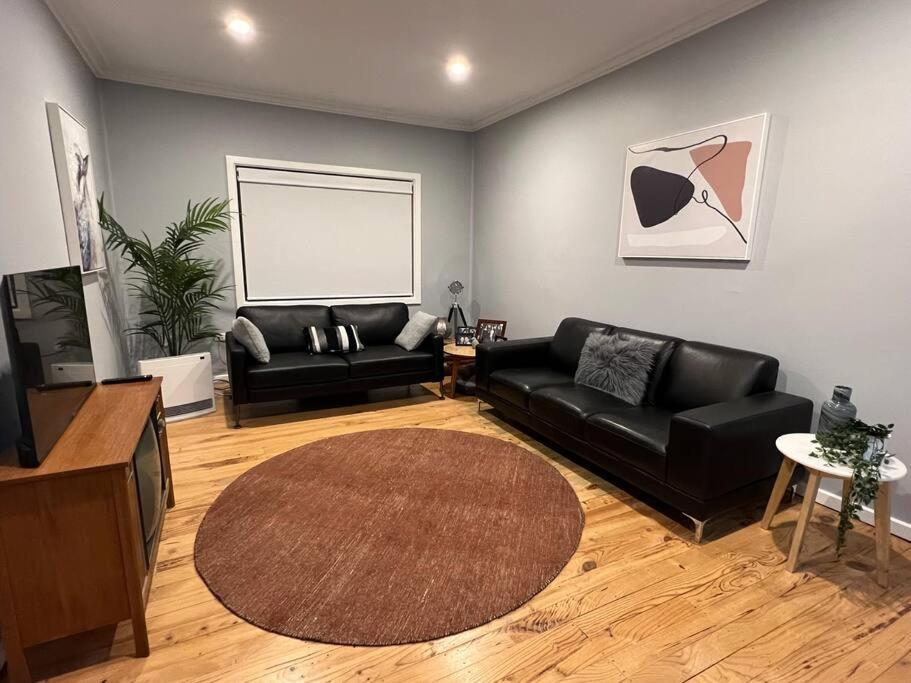 a living room with a black couch and a television at The Cottage in Queanbeyan