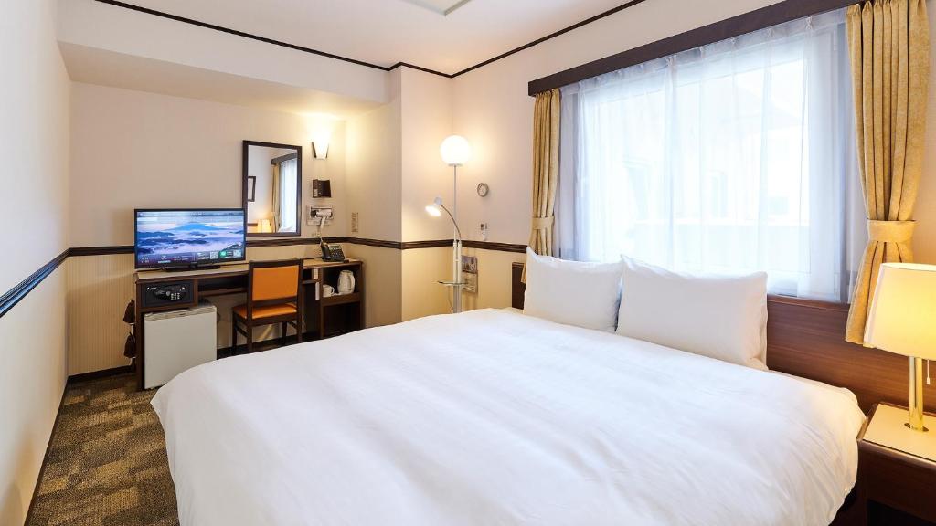 a hotel room with a white bed and a television at Toyoko Inn Osaka Itami Airport in Toyonaka