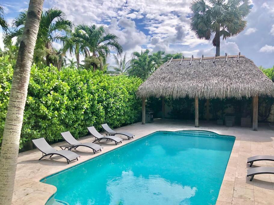 a swimming pool with chairs and a thatch roof at Villa Palma-Hollywood Beach - Summer Getaway! in Hollywood