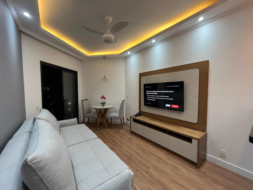 uma sala de estar com um sofá branco e uma televisão de ecrã plano em Flat Premium -Acesso a pé ao shopping Center vale - Edifício Summit (Ar condicionado) em São José dos Campos