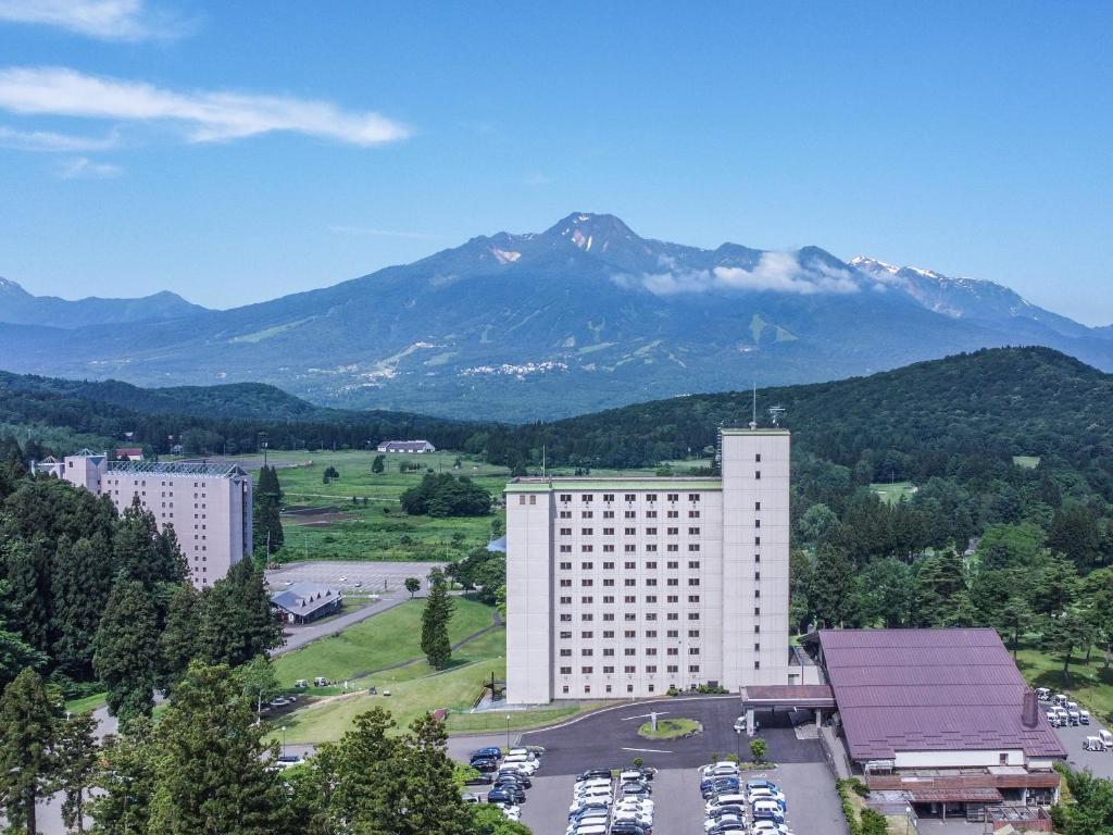 a large white building with a mountain in the background at APA Hotel & Resort Joetsu Myoko in Myoko