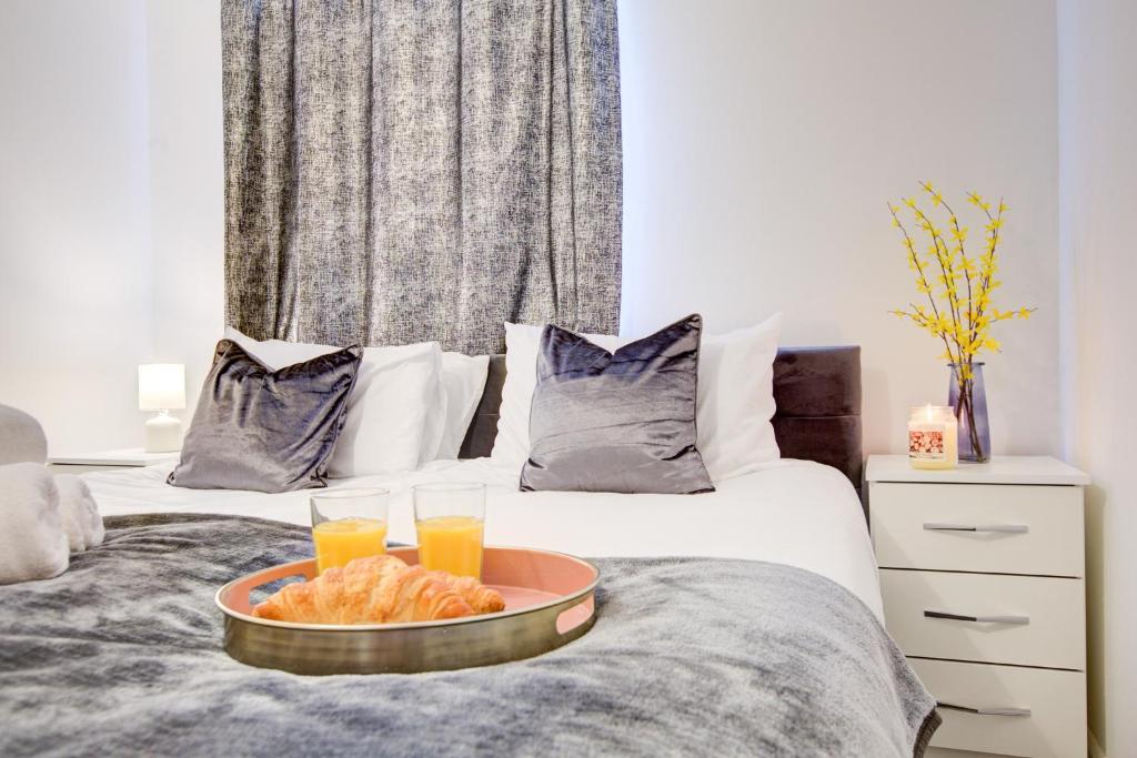 a tray of food on a bed with two glasses of orange juice at Inviting Urban Apartment in Croydon in Croydon