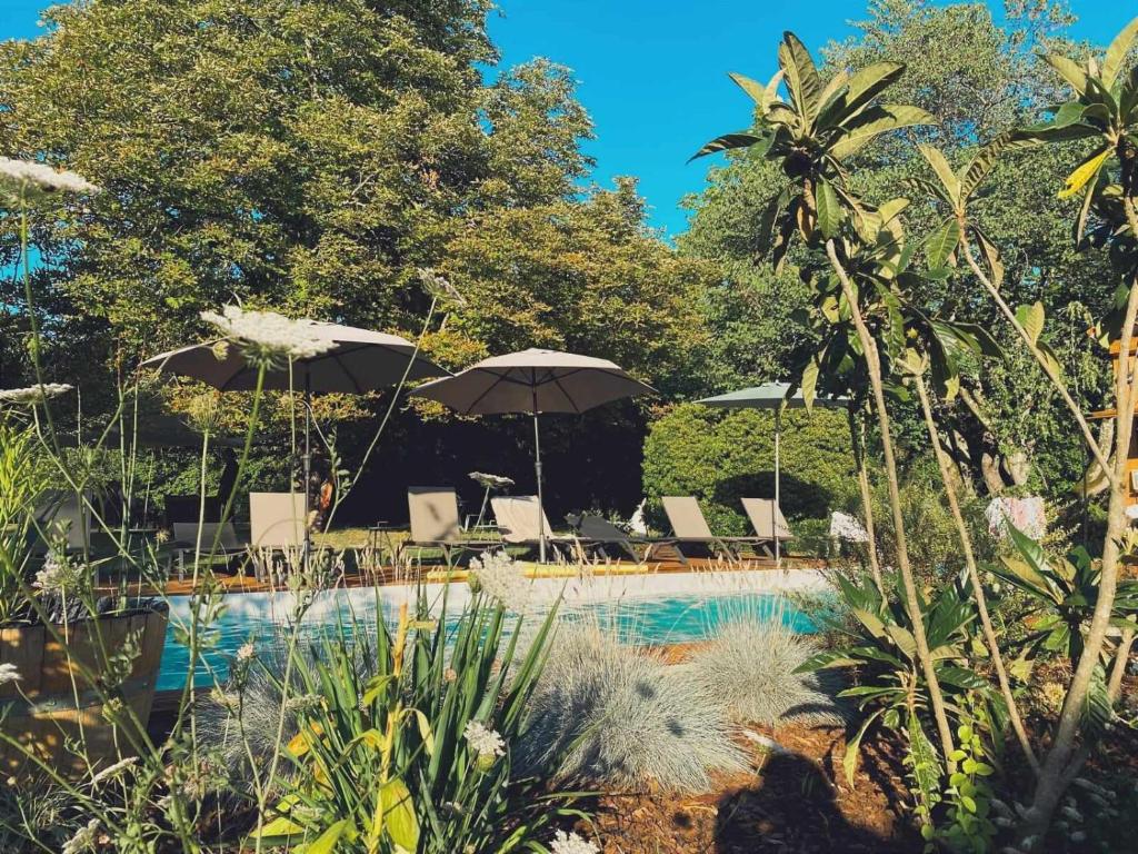 a swimming pool with umbrellas and chairs next to a pool at NAMASTE COTTAGE in Issigeac