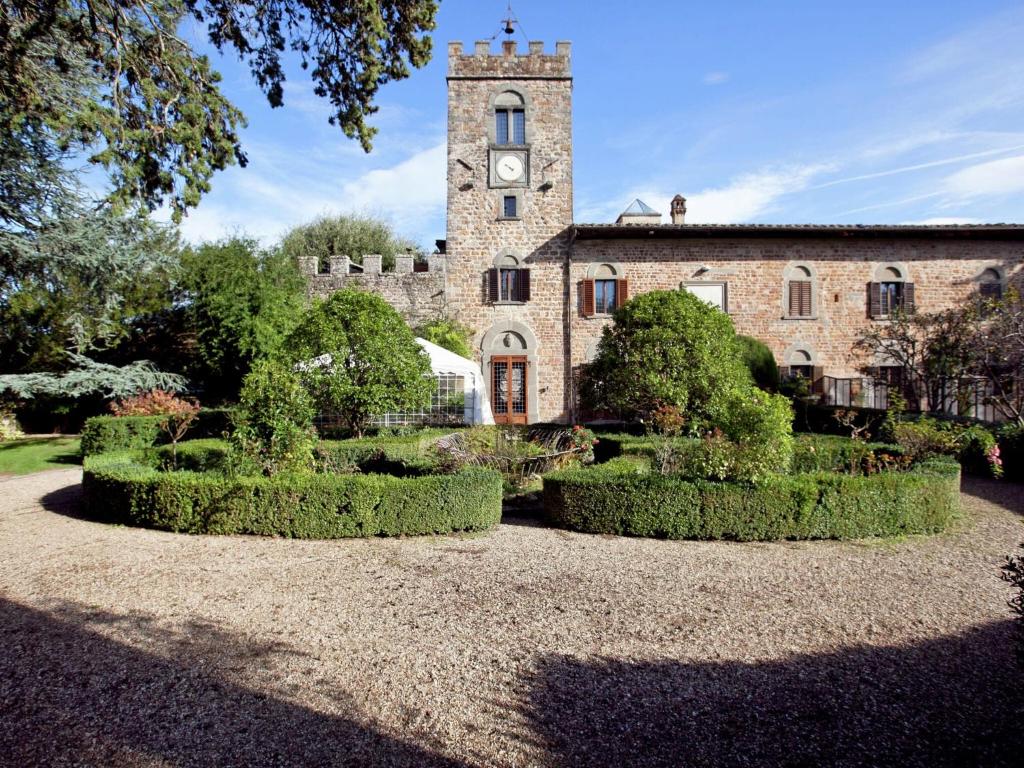 un antiguo edificio de piedra con una torre de reloj y arbustos en Pleasant Apartment with Swimming Pool Garden BBQ Parking, en Lucolena in Chianti