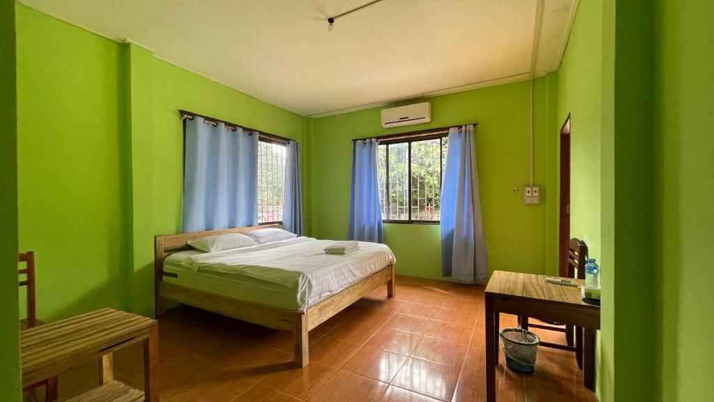 a green bedroom with a bed and a table at sokxay guerthouse in Vang Vieng