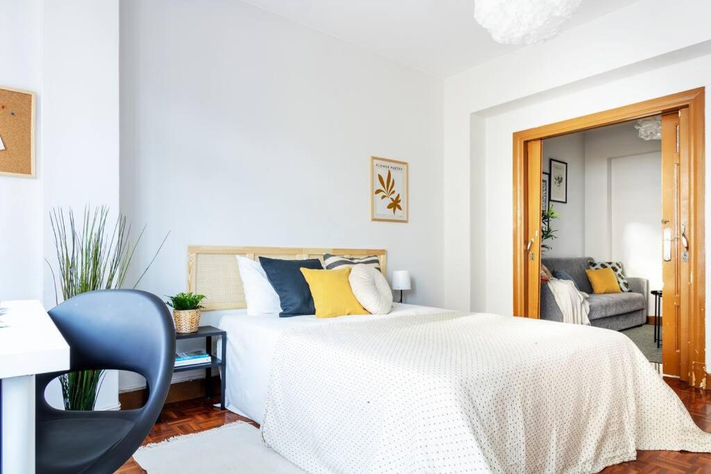 a white bedroom with a bed and a blue chair at VibesCoruna - Outeiro 222 in A Coruña