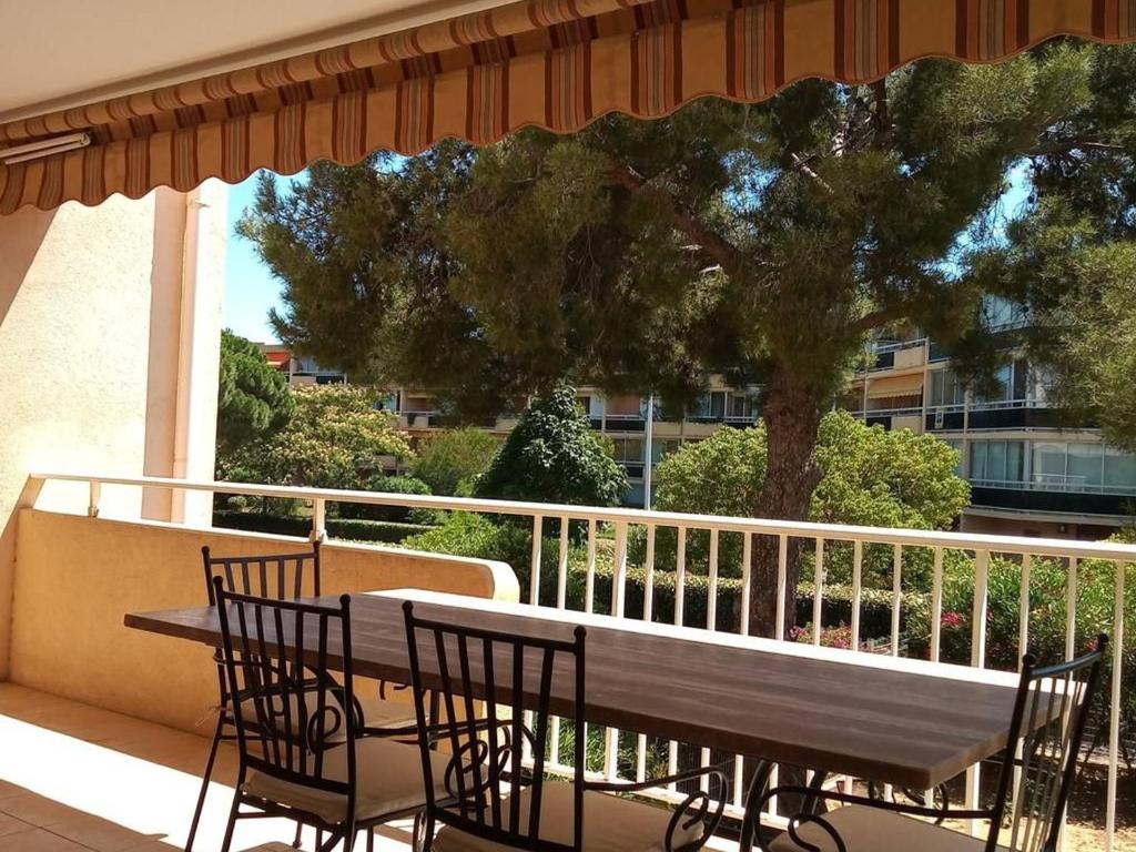 ein Holztisch und Stühle auf einem Balkon mit einem Baum in der Unterkunft T3 68m², 4*, climatisé avec loggia, proche mer et commerces – Bormes-les-Mimosas - FR-1-610-14 in Bormes-les-Mimosas