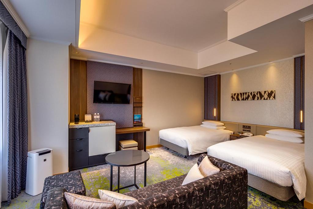 a hotel room with two beds and a couch at Hotel Nikko Kumamoto in Kumamoto