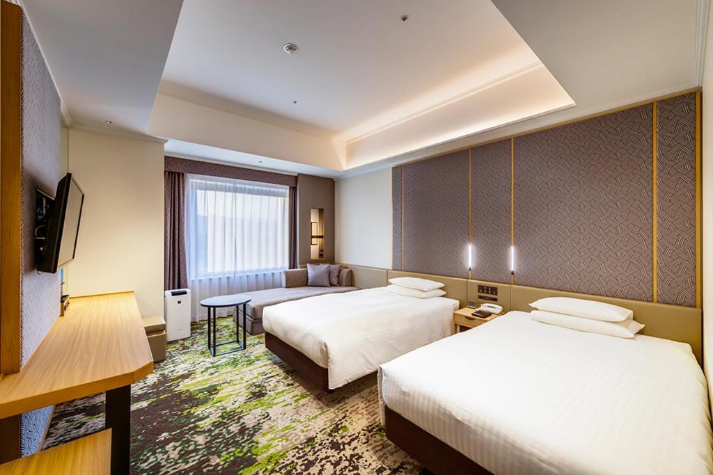 a hotel room with two beds and a television at Hotel Nikko Kumamoto in Kumamoto