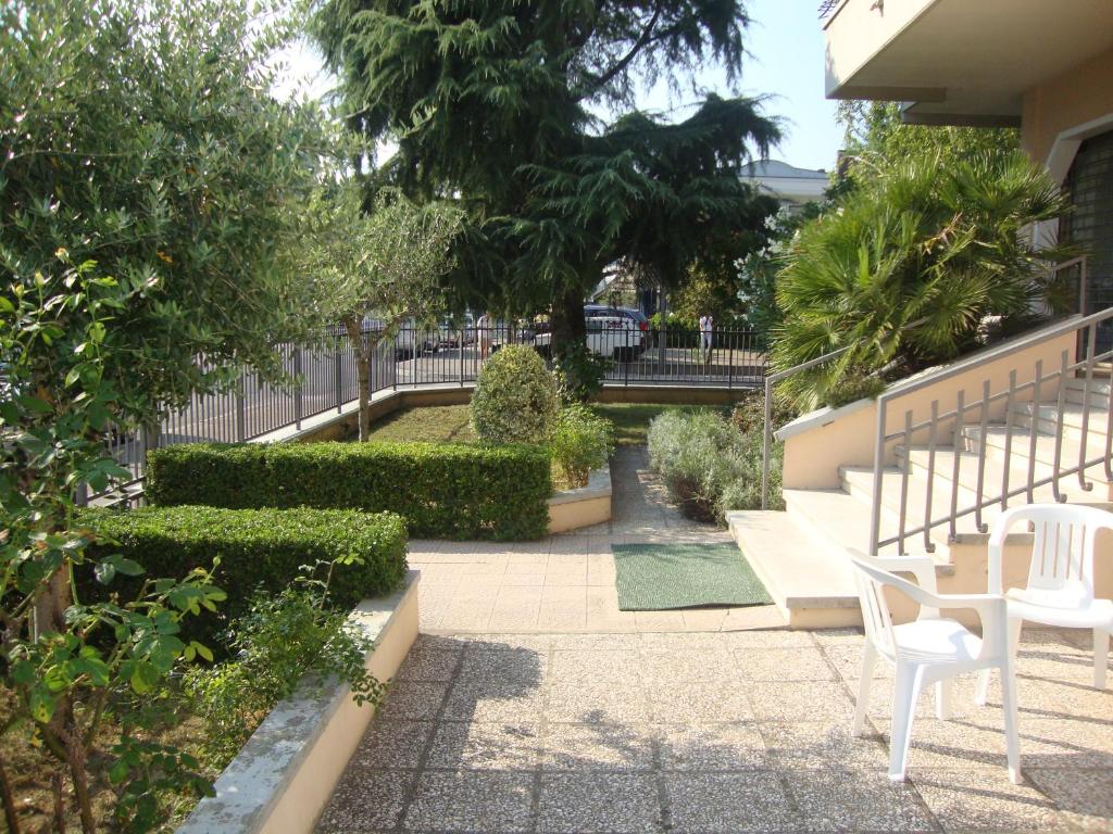 een patio met witte stoelen en bomen en een hek bij Appartamenti MOTIV Riccione in Riccione