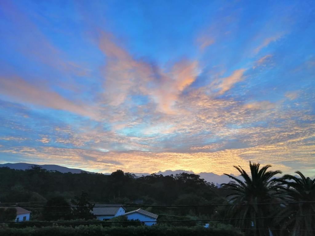 um céu nublado ao pôr do sol com casas e árvores em Quinta das Perdizes - Low Cost em Ponta Delgada