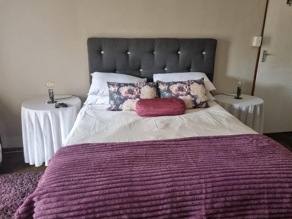 - un grand lit avec une couette violette et 2 tables dans l'établissement Guest Room, à Boksburg