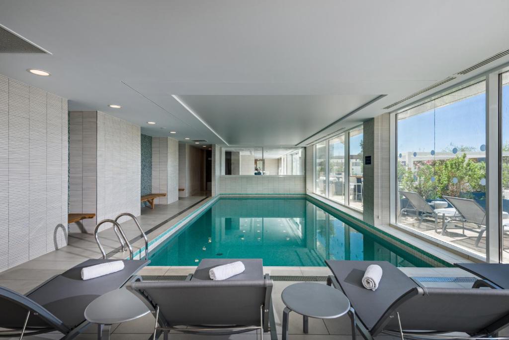 a swimming pool in a building with chairs and windows at Golden Tulip Marseille Euromed in Marseille