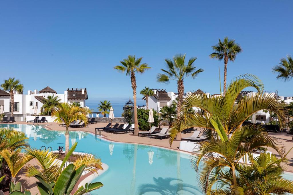 a large swimming pool with palm trees and the ocean at Las Terrazas de Abama Suites in Guía de Isora