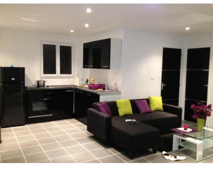 ein Wohnzimmer mit einem schwarzen Sofa und einer Küche in der Unterkunft Hollidays home piscine et jardin in Plan-de-Cuques