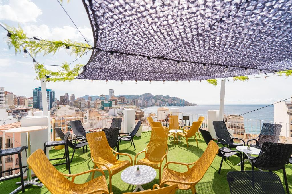 un patio en la azotea con sillas y mesas y vistas a la ciudad en Hotel Queens - Adults Only, en Benidorm