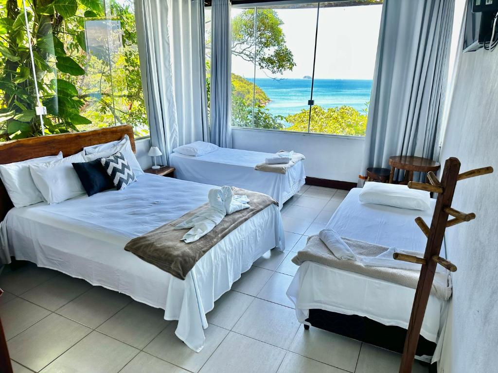 two beds in a room with a view of the ocean at OYO Deck Da Villa Pousada Hotel in Picinguaba