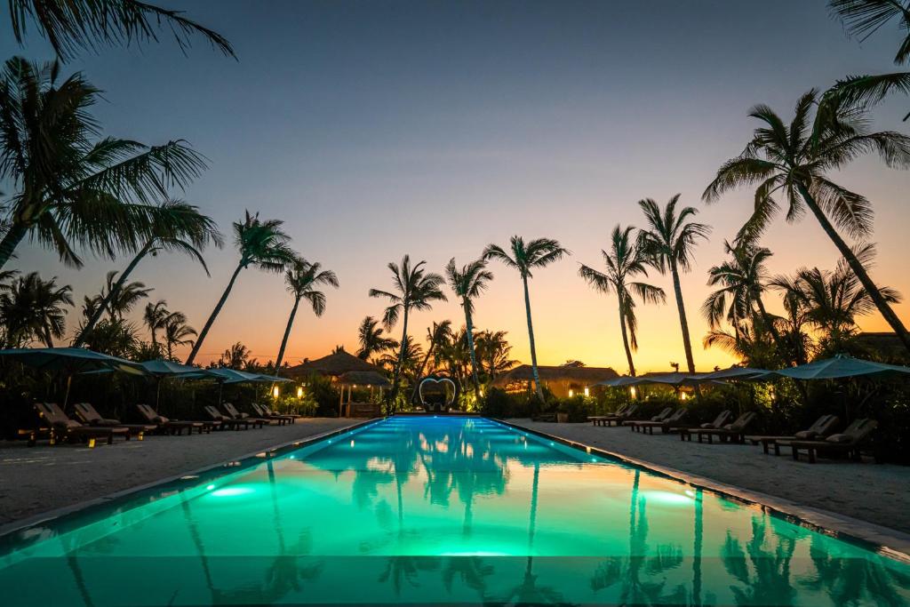 une piscine dans un complexe avec des palmiers et un coucher de soleil dans l'établissement Sensations Eco-Chic Hotel, à Pwani Mchangani Mdogo